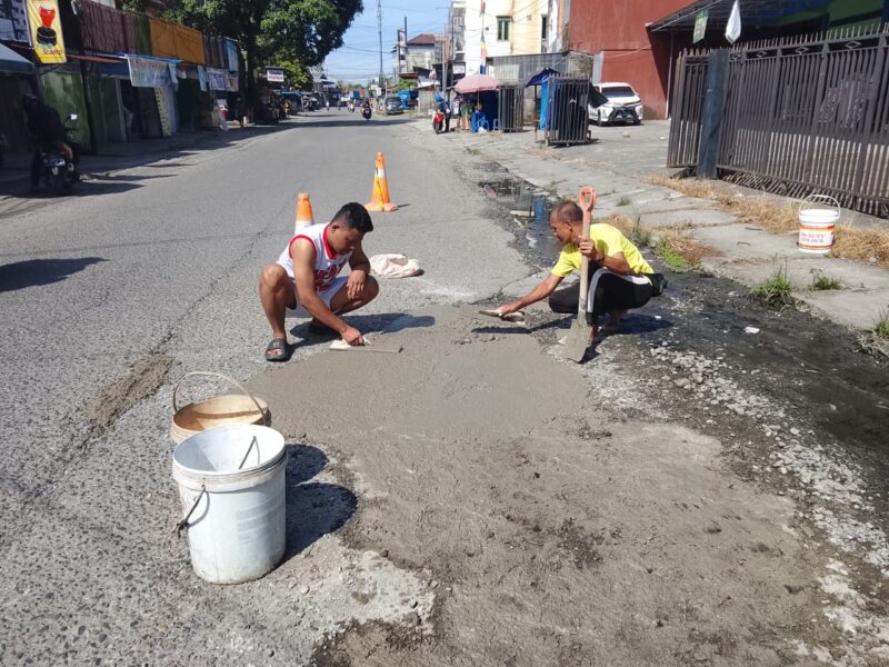 Warga menambal jalan berlubang secara swadaya di Jalan Pendidikan Jalur 1, Kelurahan Otomona, Timika, Minggu (21/12).